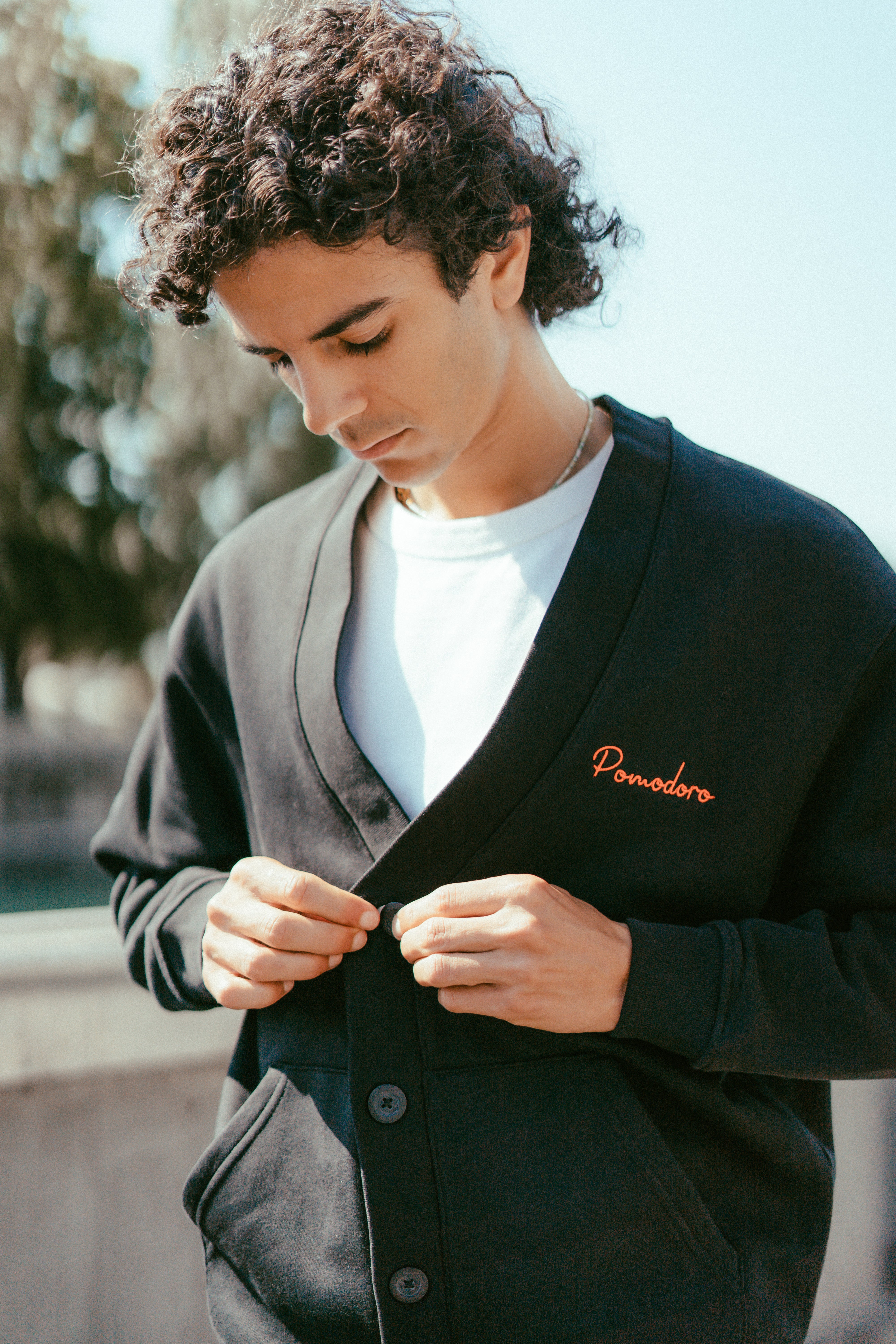 Cardigan noir unisexe porté par un modèle, coupe oversize avec broderie en rouge, avec logo Pomodoro, côté cœur.