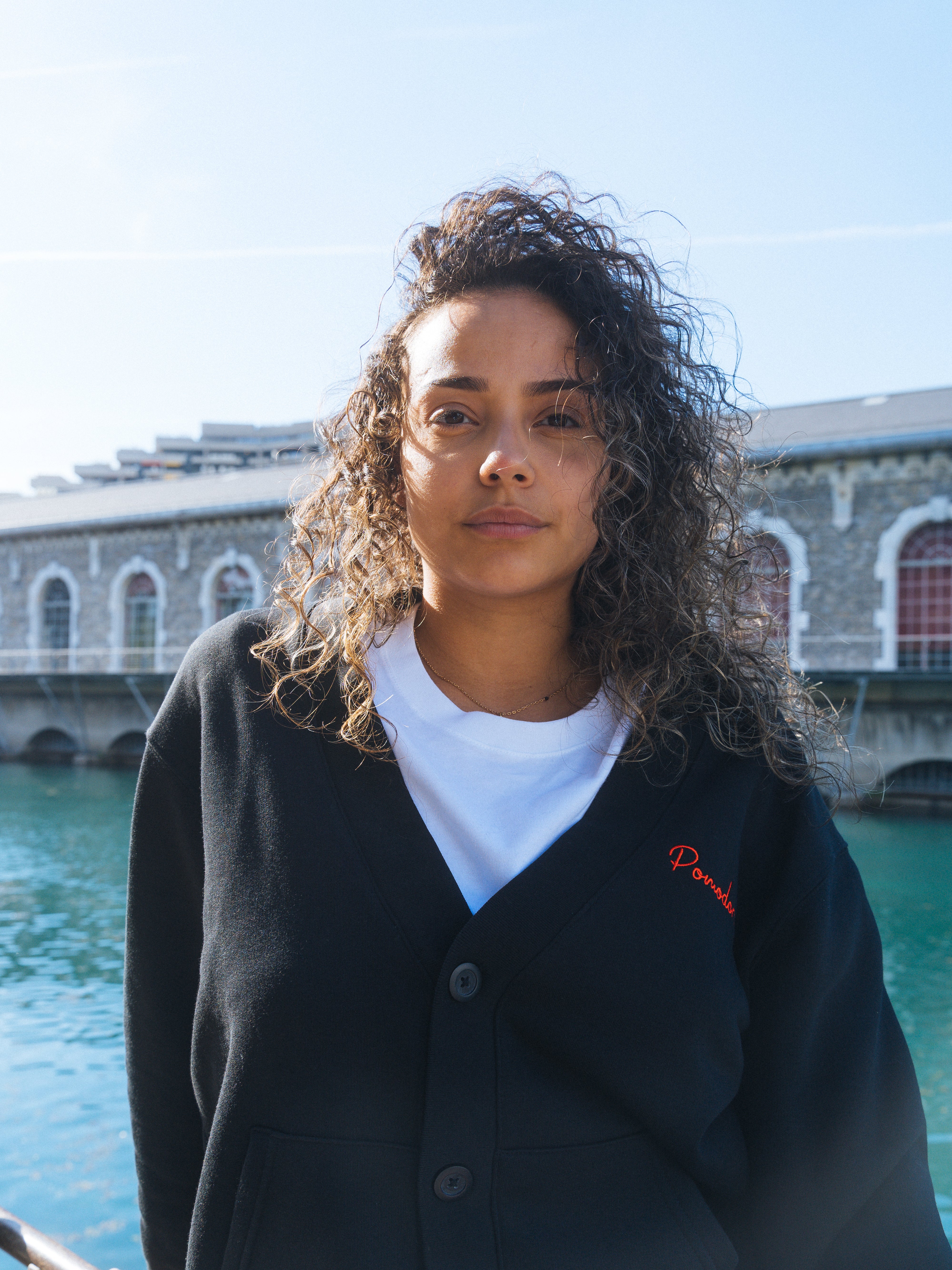 Cardigan noir unisexe porté par une modèle, coupe oversize avec broderie en rouge, avec logo Pomodoro, côté cœur.